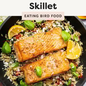 Salmon filets in a skillet over veggie-packed orzo.