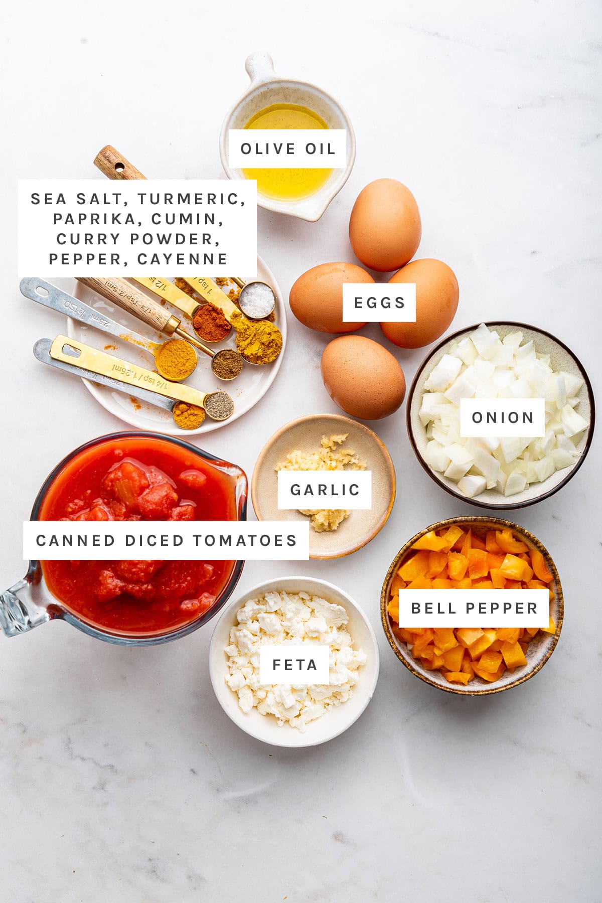 Ingredients measured out to make Shakshuka: olive oil, sea salt, turmeric, paprika, cumin, curry powder, pepper, cayenne, garlic, onion, canned diced tomatoes, feta and bell pepper.