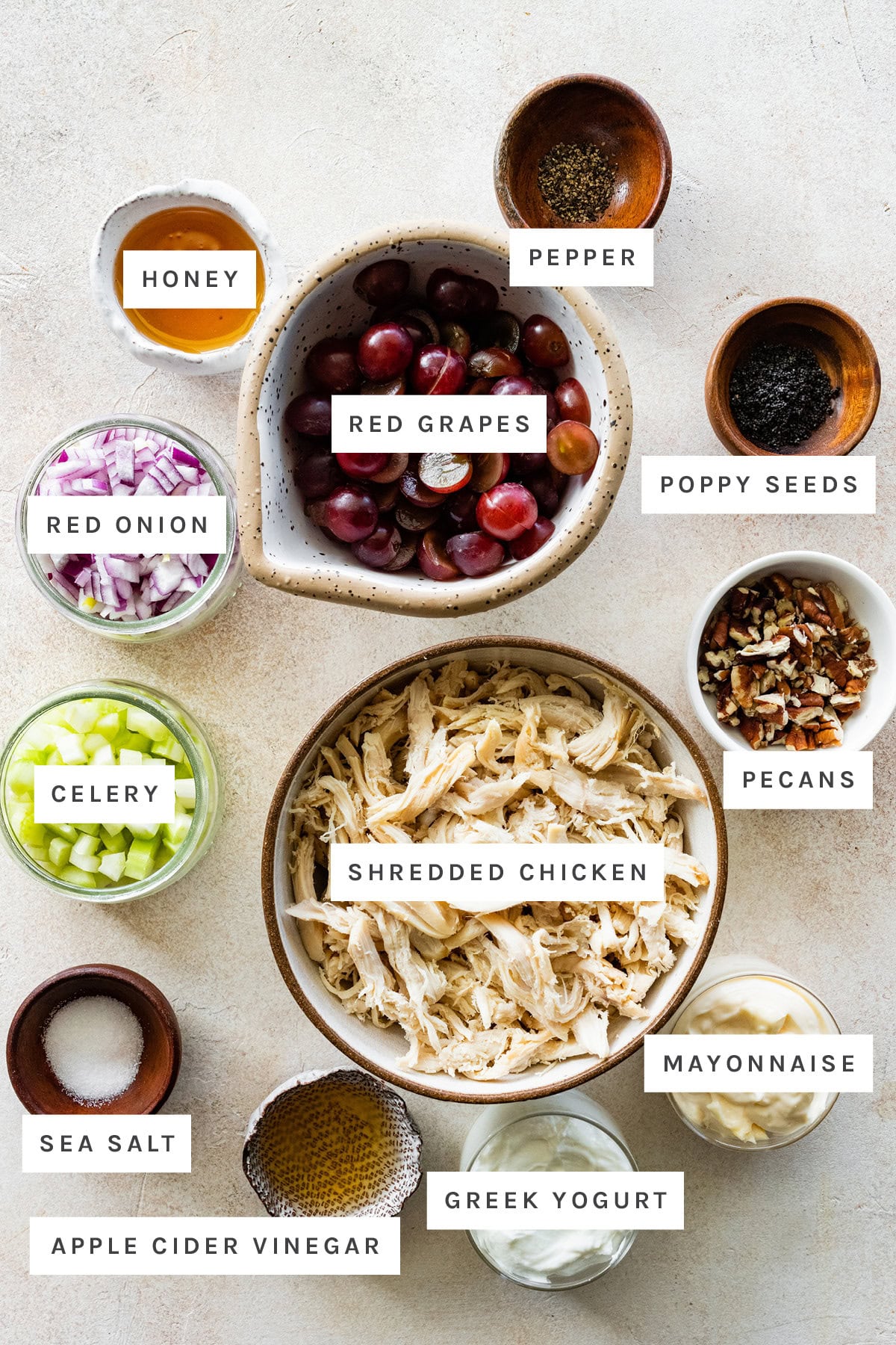 Ingredients measured out to make Sonoma Chicken Salad: honey, pepper, red grapes, poppy seeds, red onion, celery, pecans, shredded chicken, sea salt, apple cider vinegar, Greek yogurt and mayonnaise.
