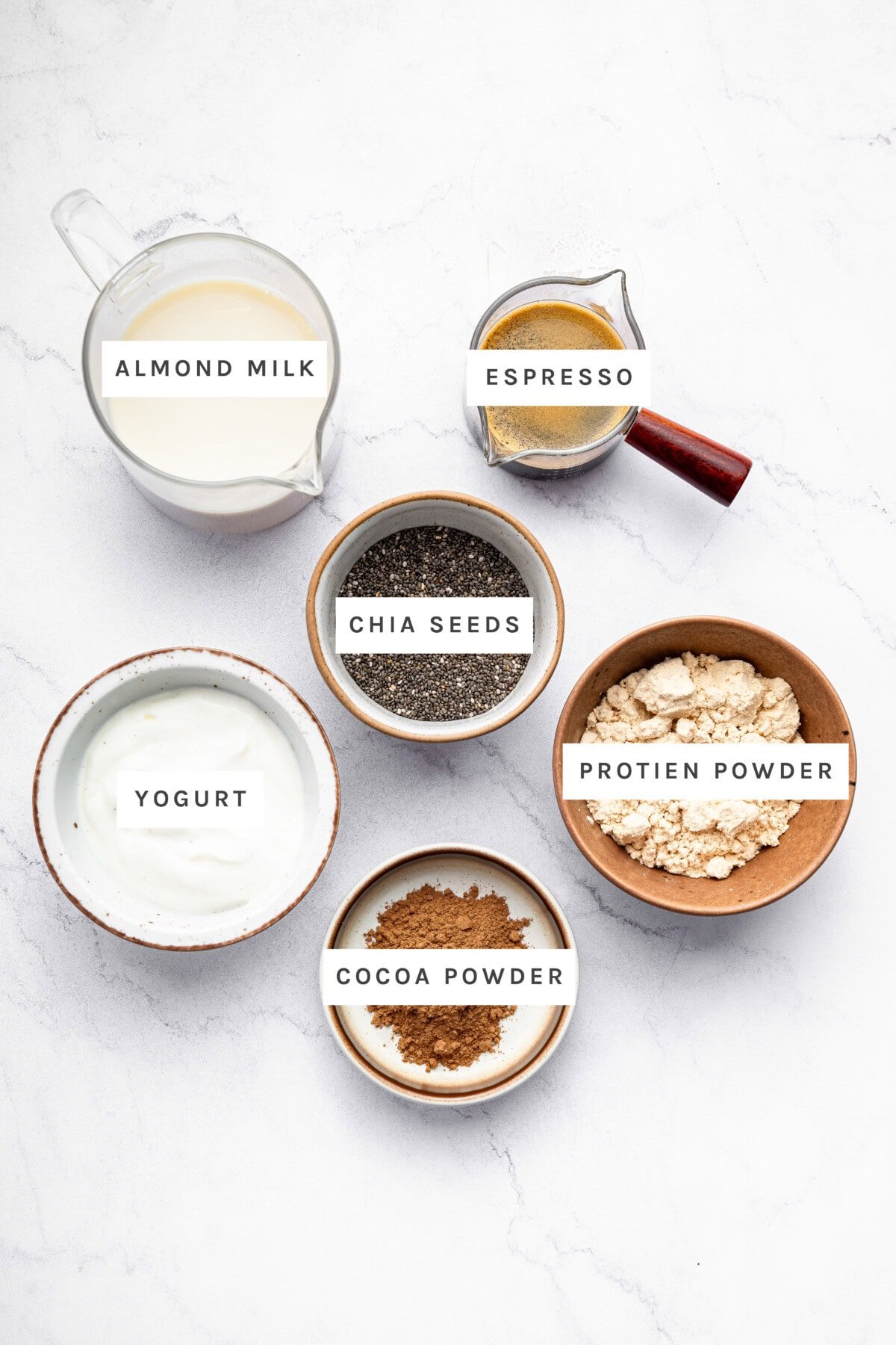 Ingredients measured out to make Tiramisu Chia Pudding: Almond milk, yogurt, cocoa powder, protein powder, espresso and chia seeds