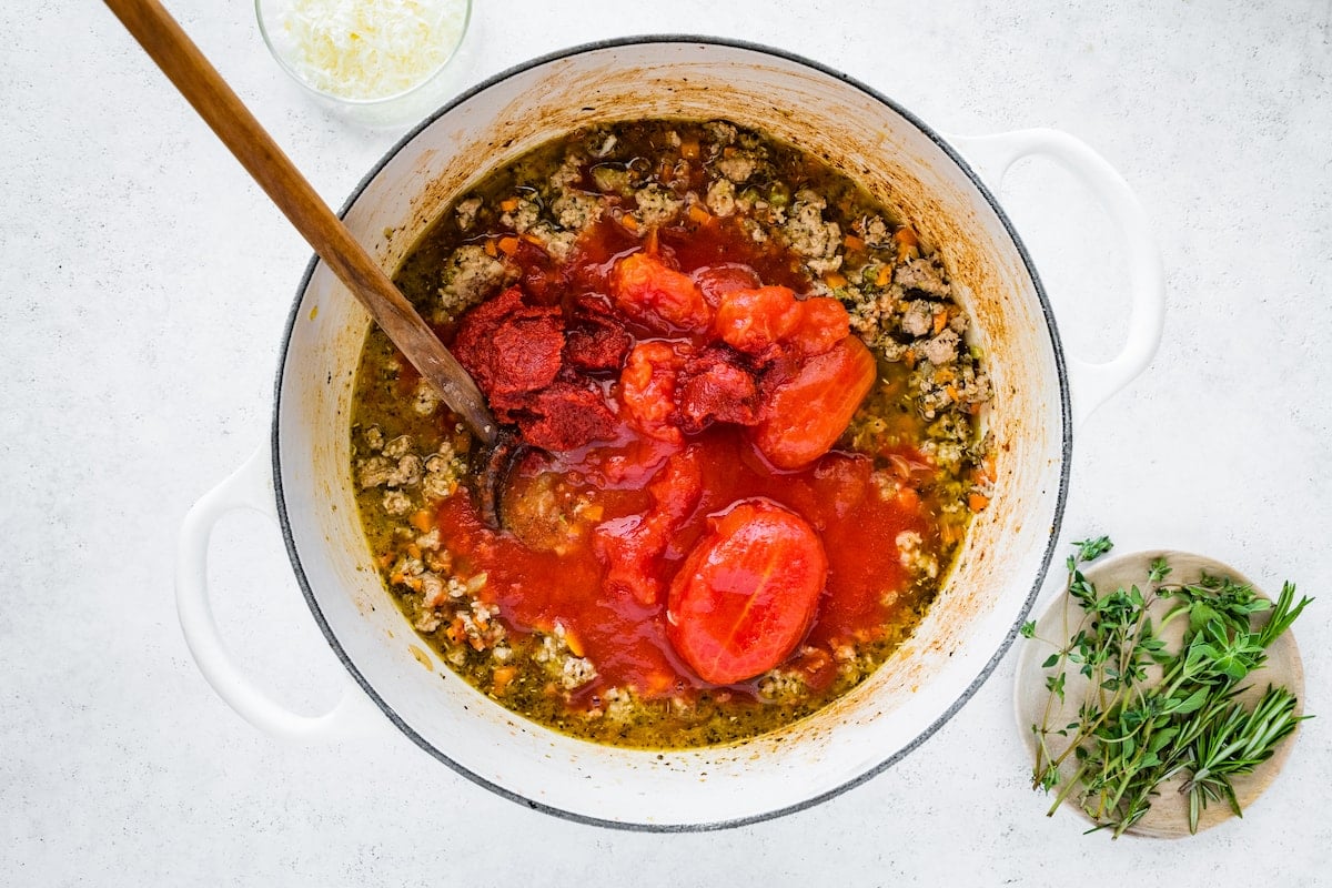 Tomatoes and tomato paste added to a large dutch oven with cooked turkey, vegetables, herbs and spices to create a turkey bolognese.