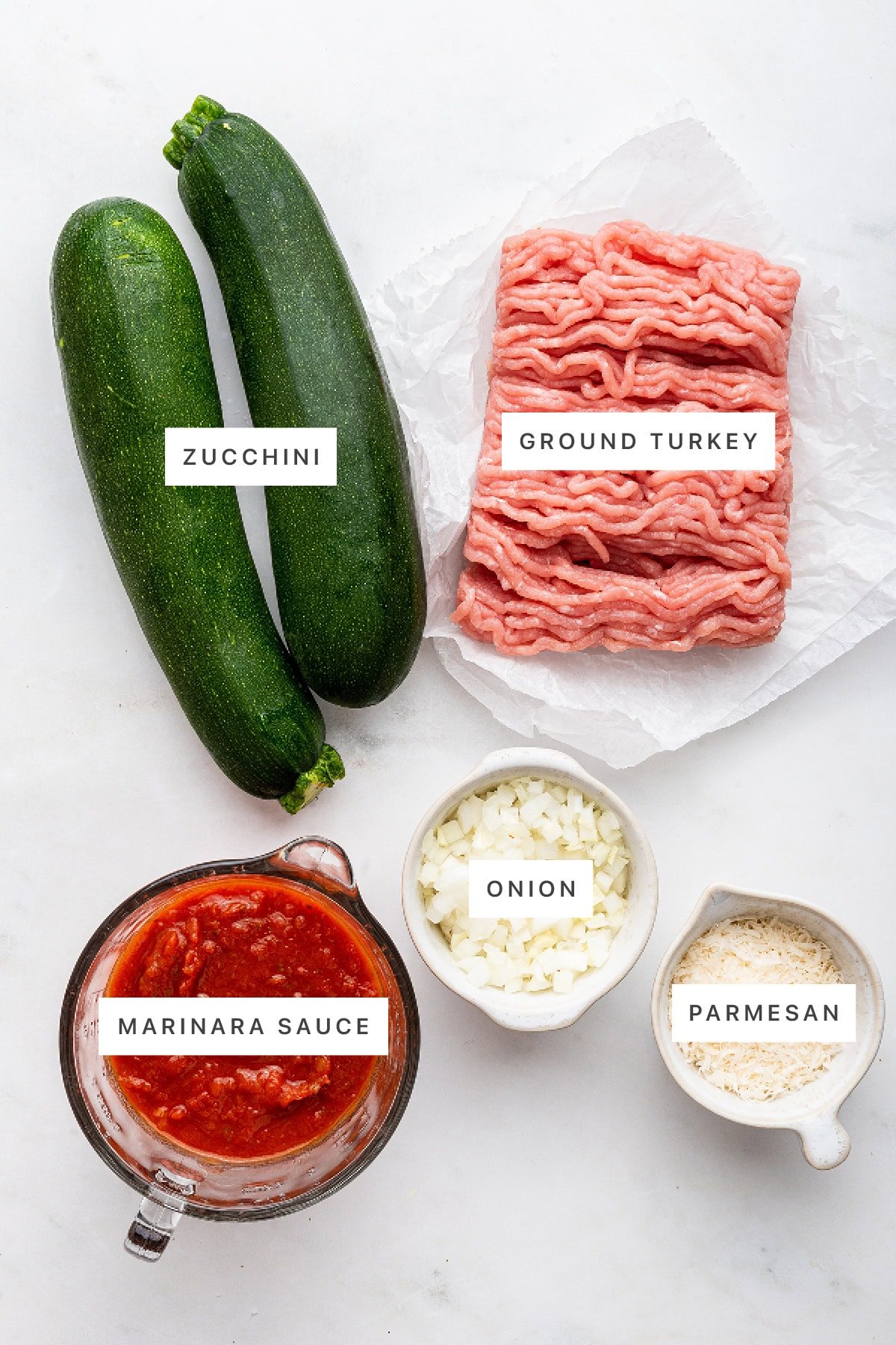 Ingredients measured out to make Turkey Zucchini Boats: zucchini, ground turkey, marinara sauce, onion and parmesan.
