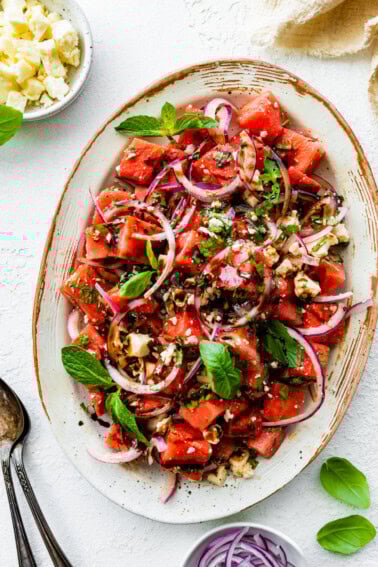 A watermelon salad with crumbled feta cheese, fresh basil, balsamic vinegar, and red onions.