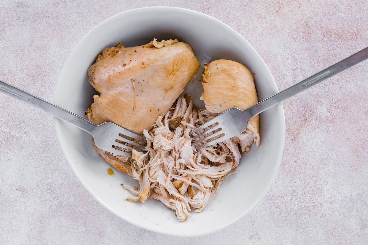 Shredding chicken in a bowl with two forks.