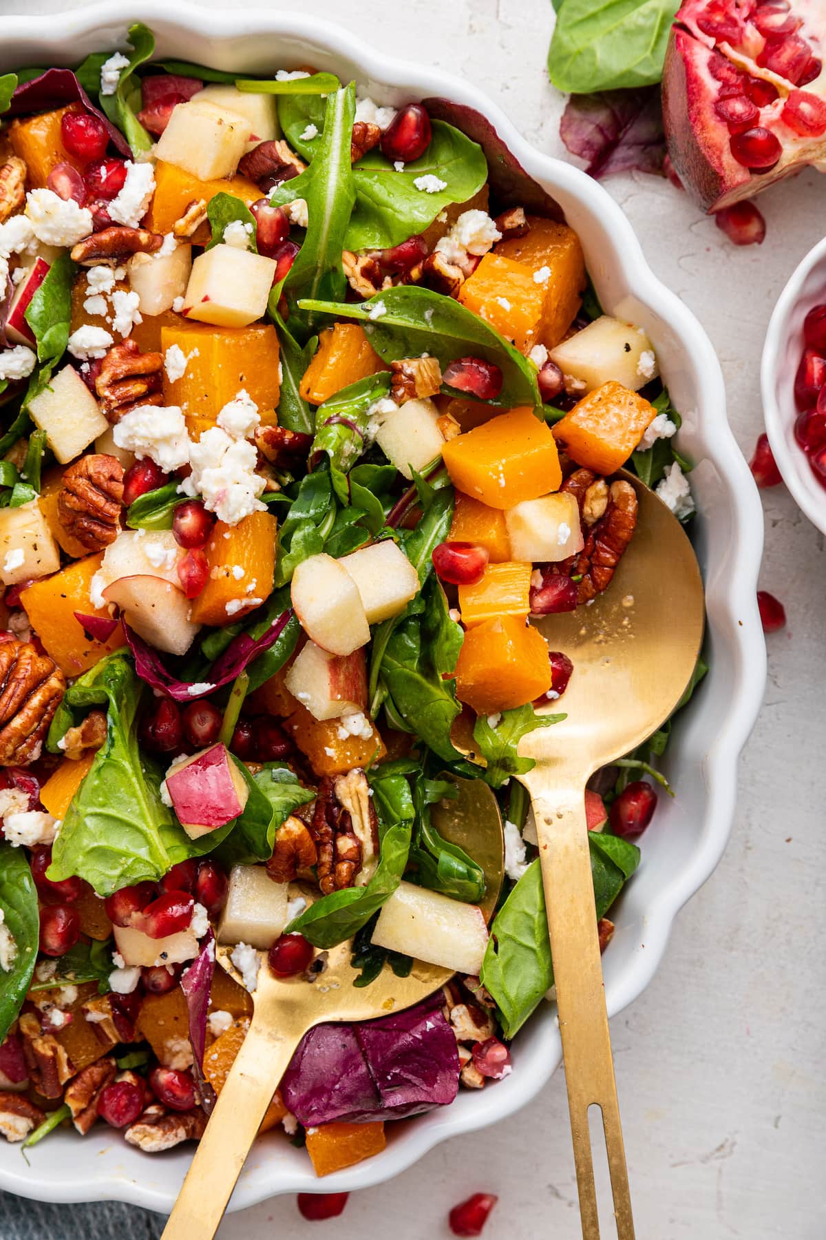 Winter salad being served in a white bowl with gold serving spoons.