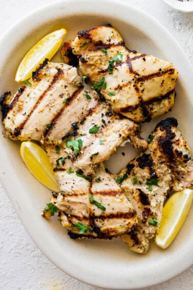 Multiple yogurt marinated chicken thighs on a plate with lemon wedges on the side.