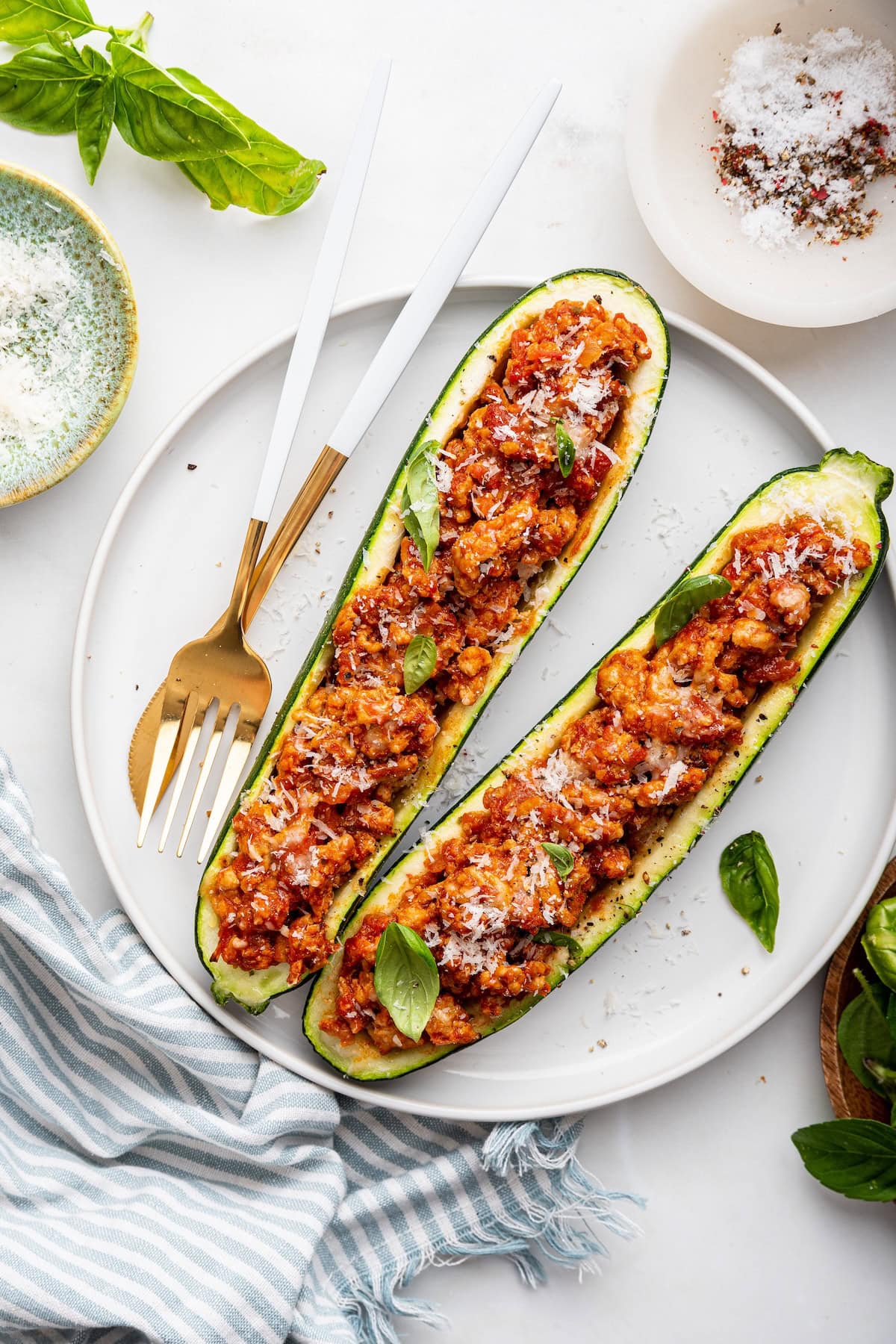 Two turkey zucchini boats on a white plate with a fork and a knife to the side.