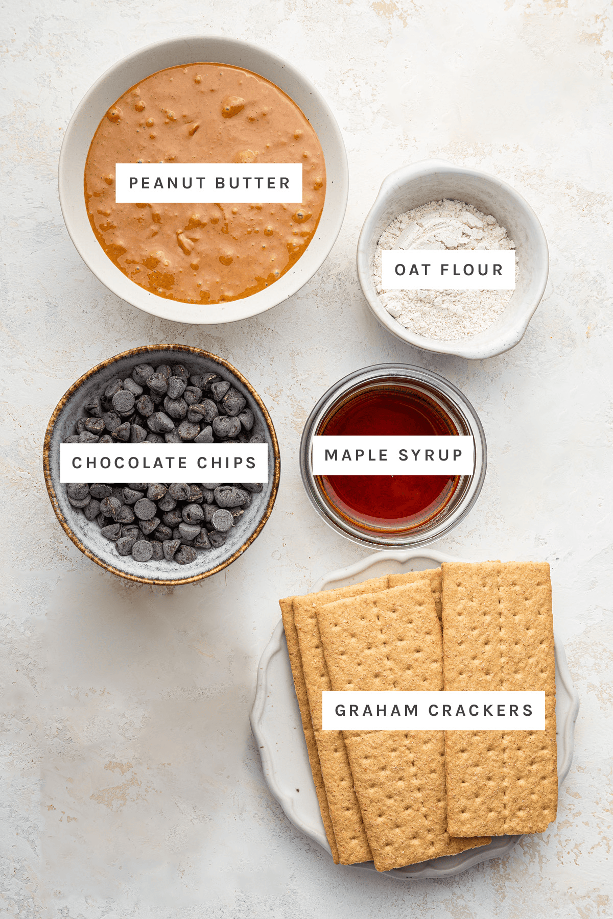 Ingredients measured out to make Healthy Peanut Butter Bars: peanut butter, oat flour, chocolate chips, maple syrup and graham crackers.